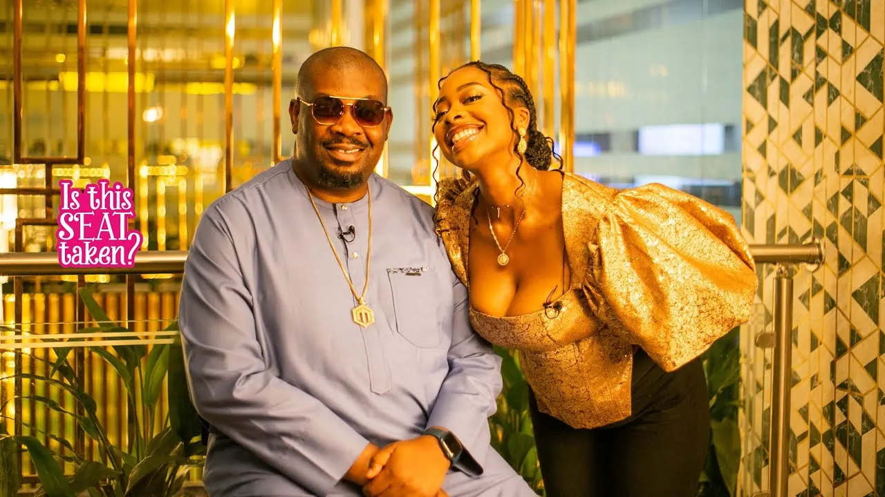 Don Jazzy and Chinasa Anukam seated beside a pink Is This Seat Taken? sign