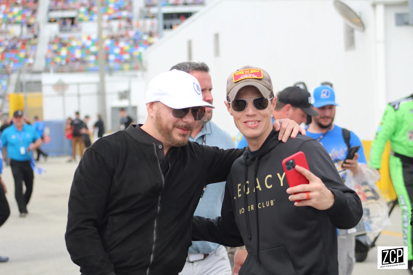 Pitbull, on the left in a white cap and dark shirt, poses for a phone photograph with another man
