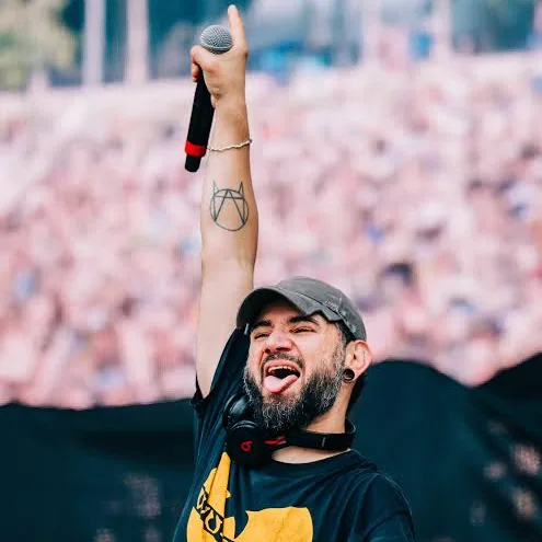 Skrillex in a grey cap and black Wu-Tang Clan T-shirt, holding a microphone above his head