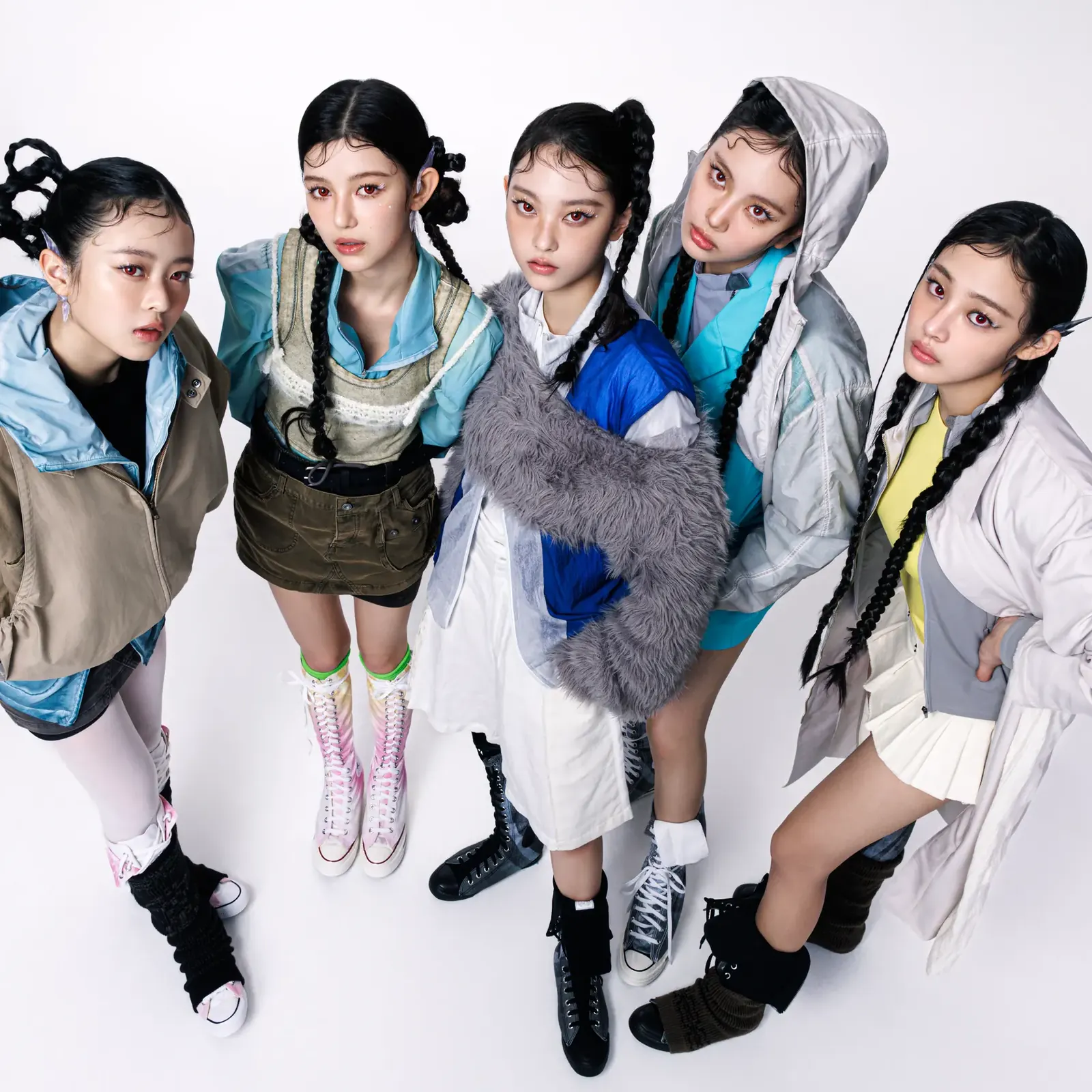 NewJeans, captioned as NJZ by Vogue Arabia, in layered outfits and braided hairstyles, photographed from above against a white studio floor