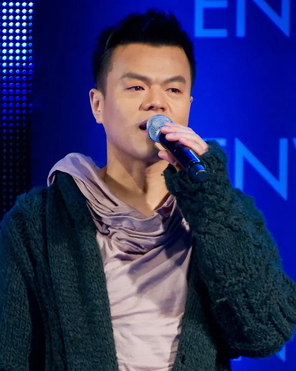 J.Y. Park, smiling, in a dark jacket at a media event