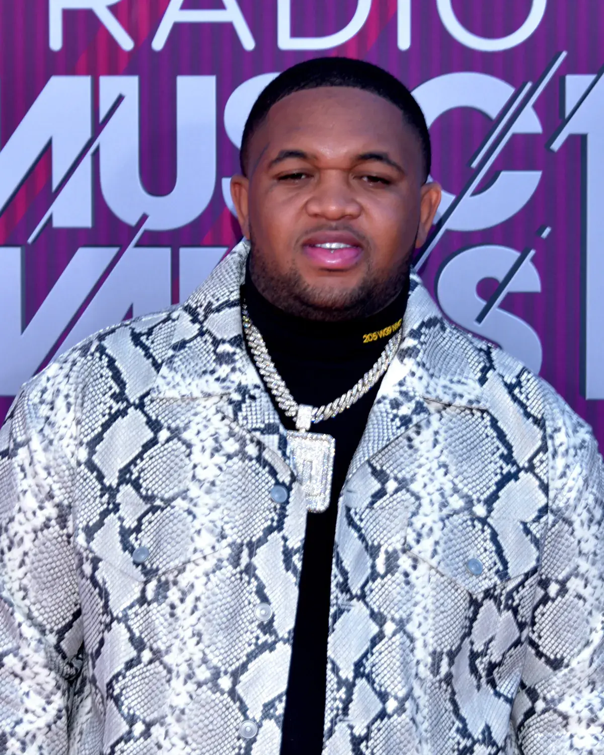 Mustard in a snakeskin-print jacket and a diamond chain on a red carpet