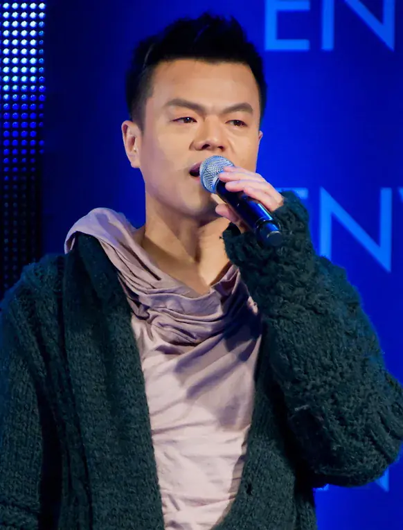 J.Y. Park sings into a microphone in front of a blue backdrop