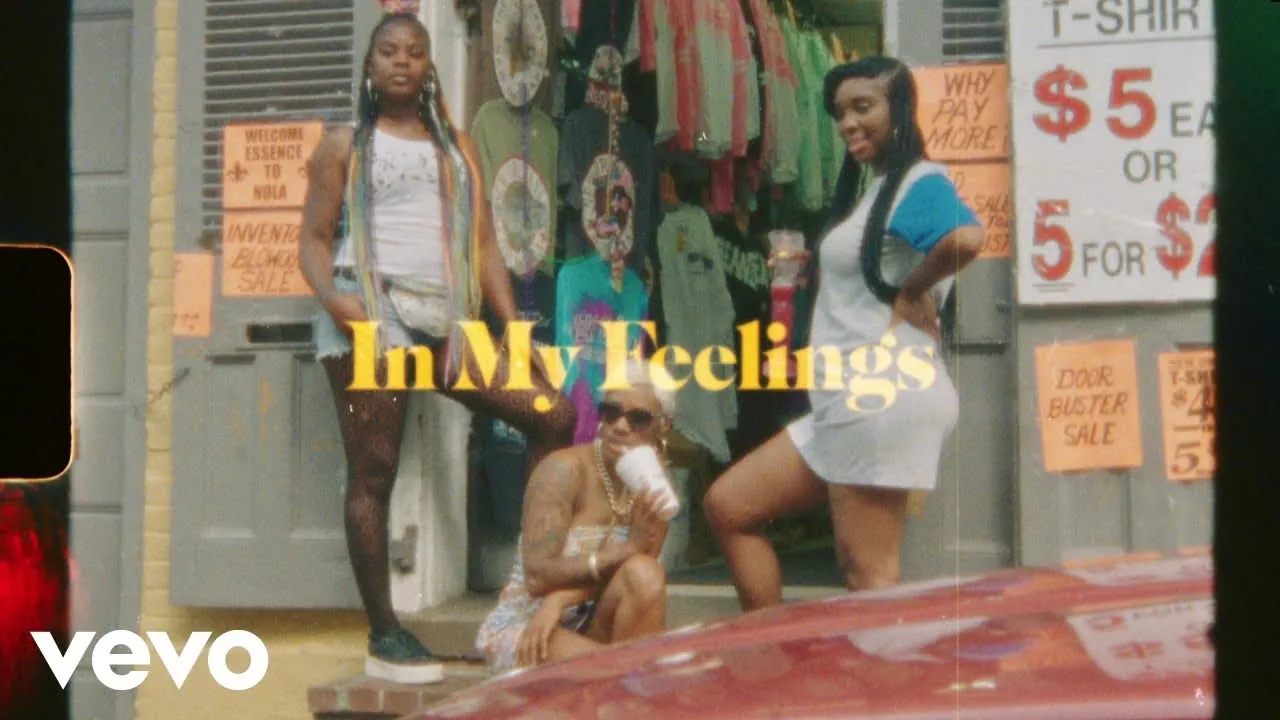 Three women posing outside a New Orleans T-shirt shop with sale signs in the window, under the title In My Feelings in yellow script