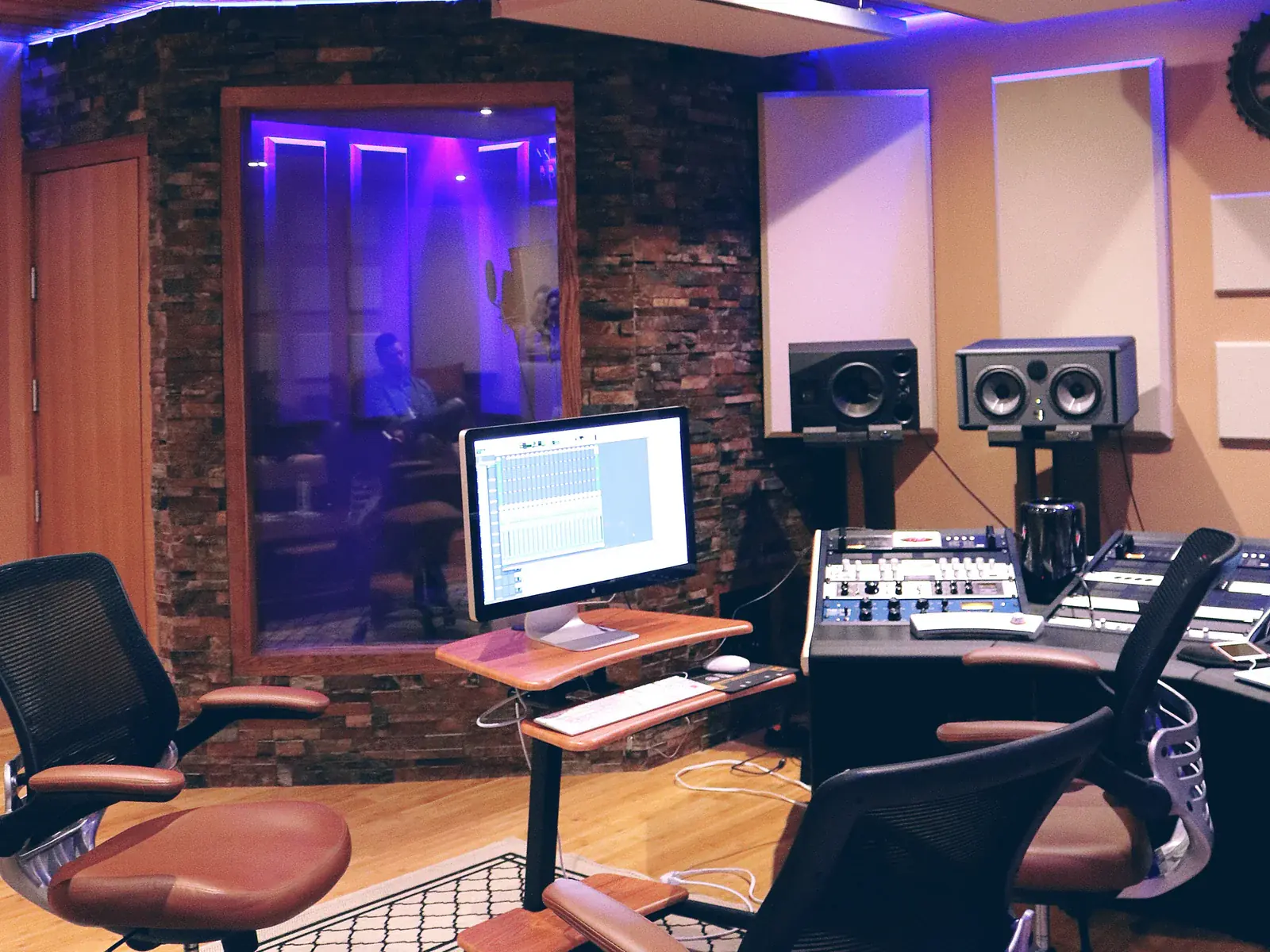 Recording workstation with studio monitors, a computer and a vocal booth behind glass