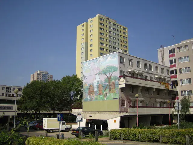 Concrete low-rise blocks and a tower on a housing estate, with a large mural of four faces on an end wall