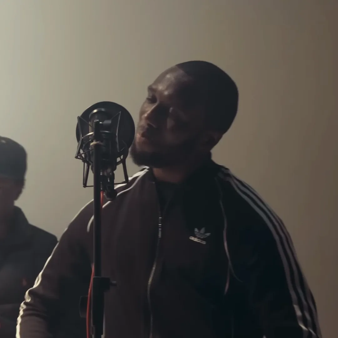 Headie One in a dark tracksuit top, eyes closed, rapping into a studio microphone with a pop filter