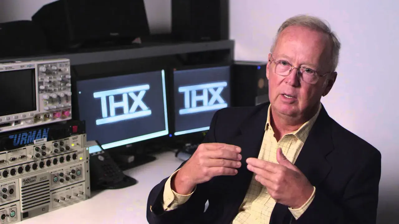 Andy Moorer speaking in a studio, with the THX logo on two monitors behind him