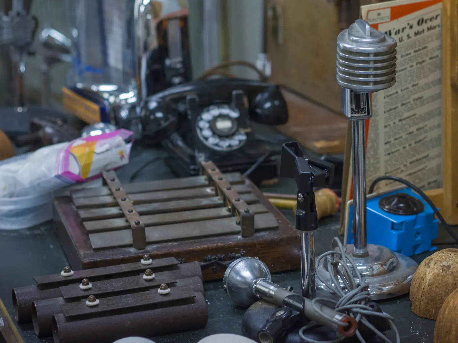 A wooden chime set, loose chime bars, a chrome microphone and a rotary telephone on a museum shelf